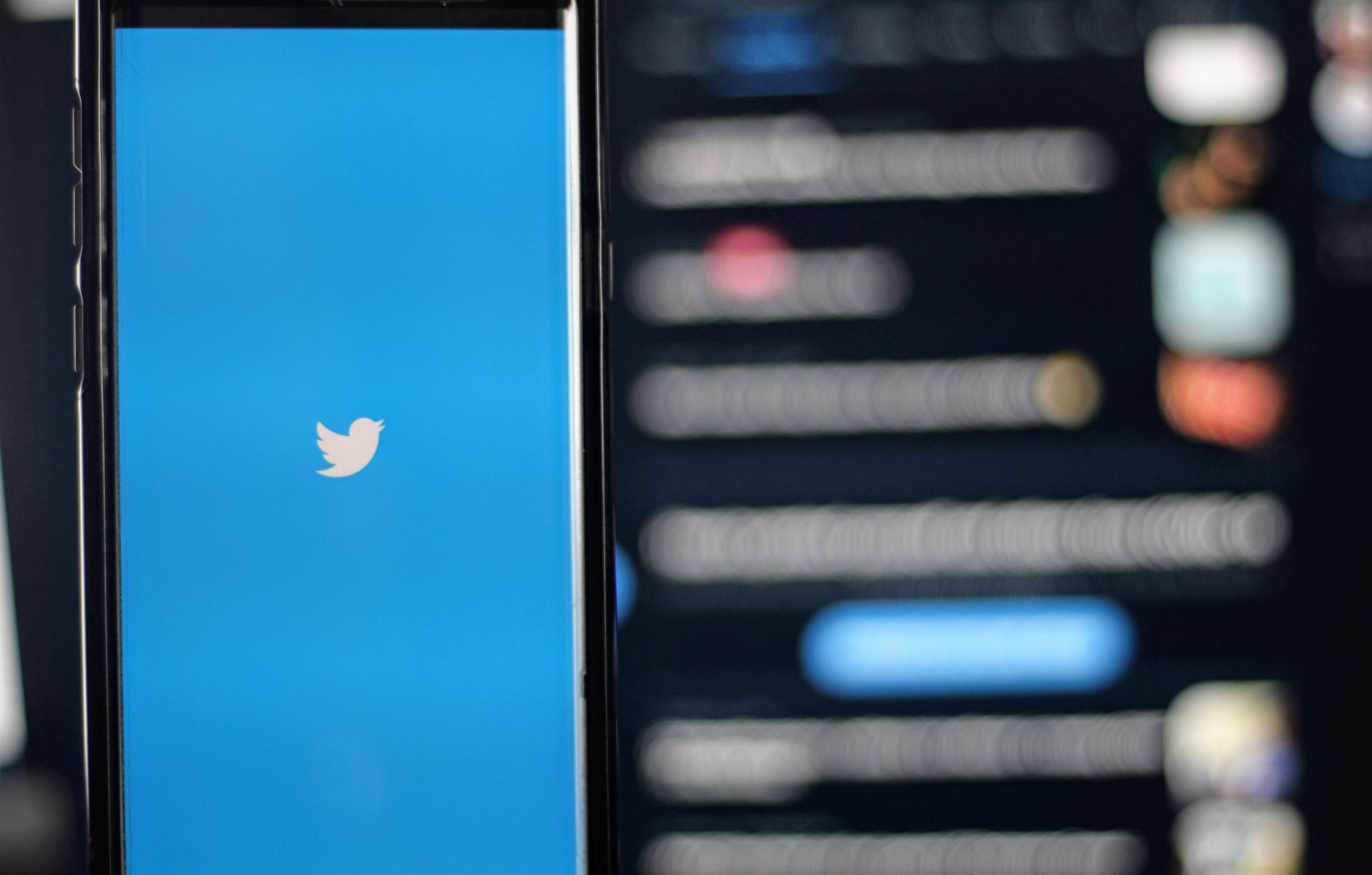 photo of a phone showing twitter, with Elon Musk's Twitter in the background