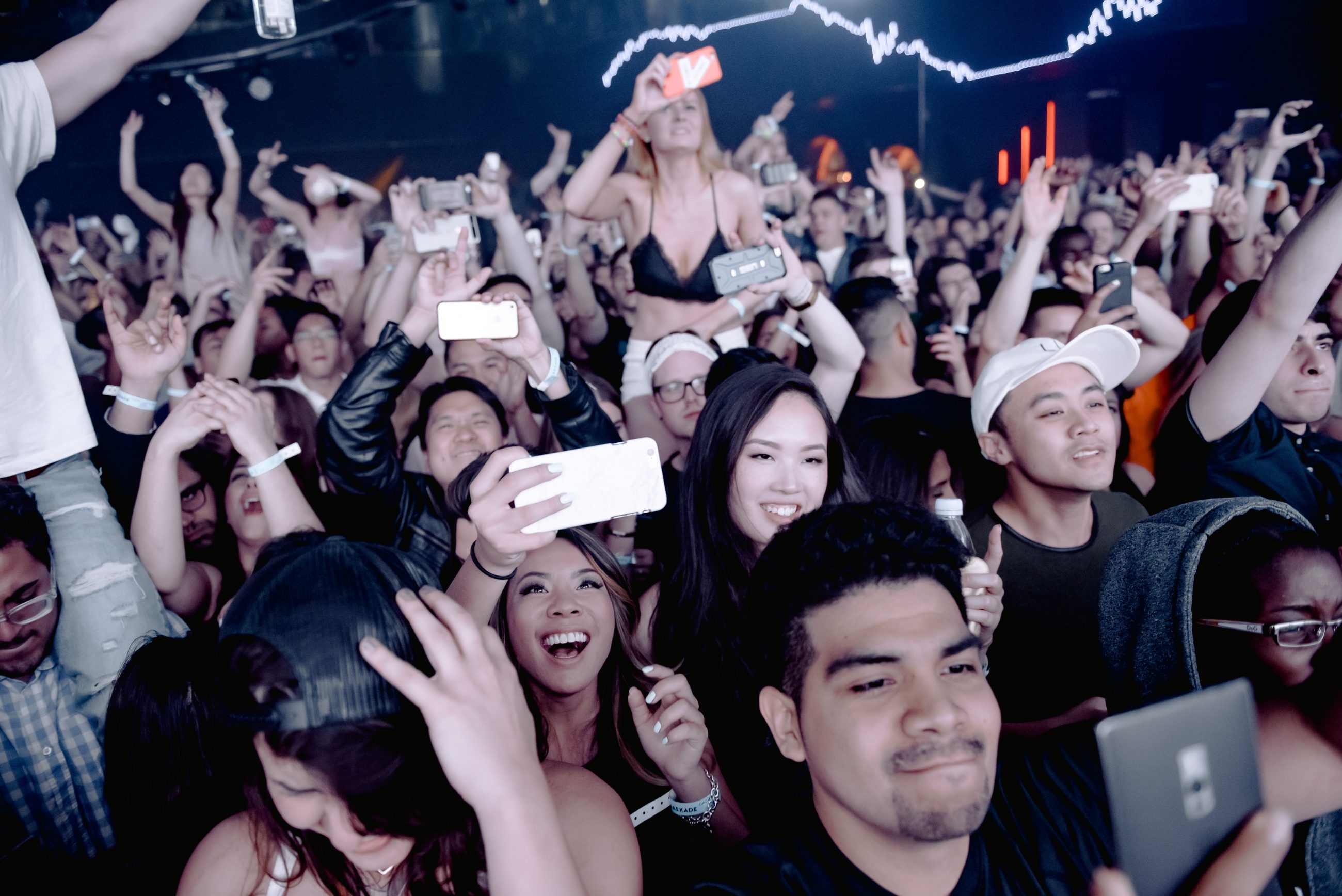 A group of people smile at a concert, with some of them holding cameras. 