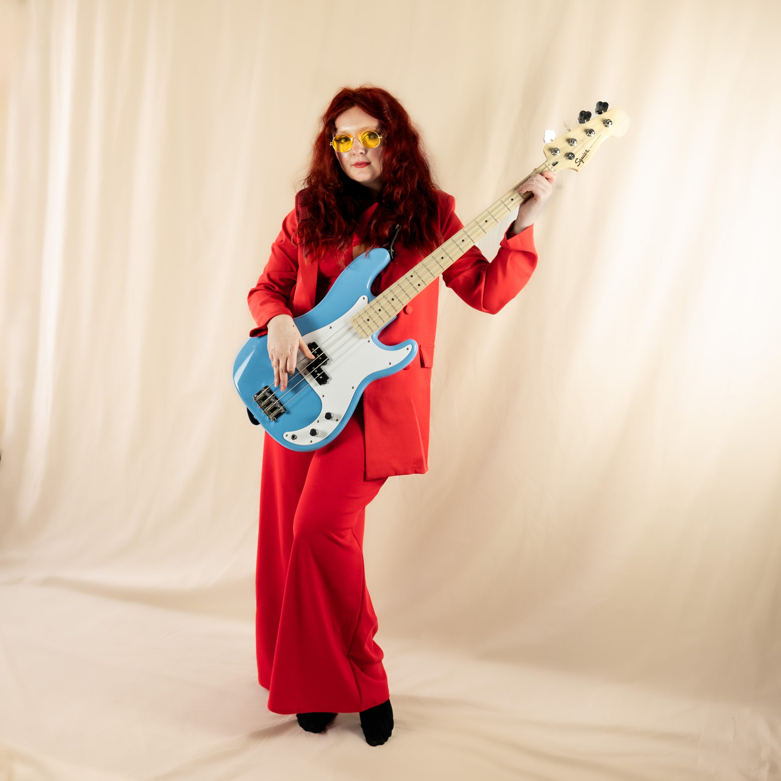 press shot of megan black, wearing a red top and pants, playing bass