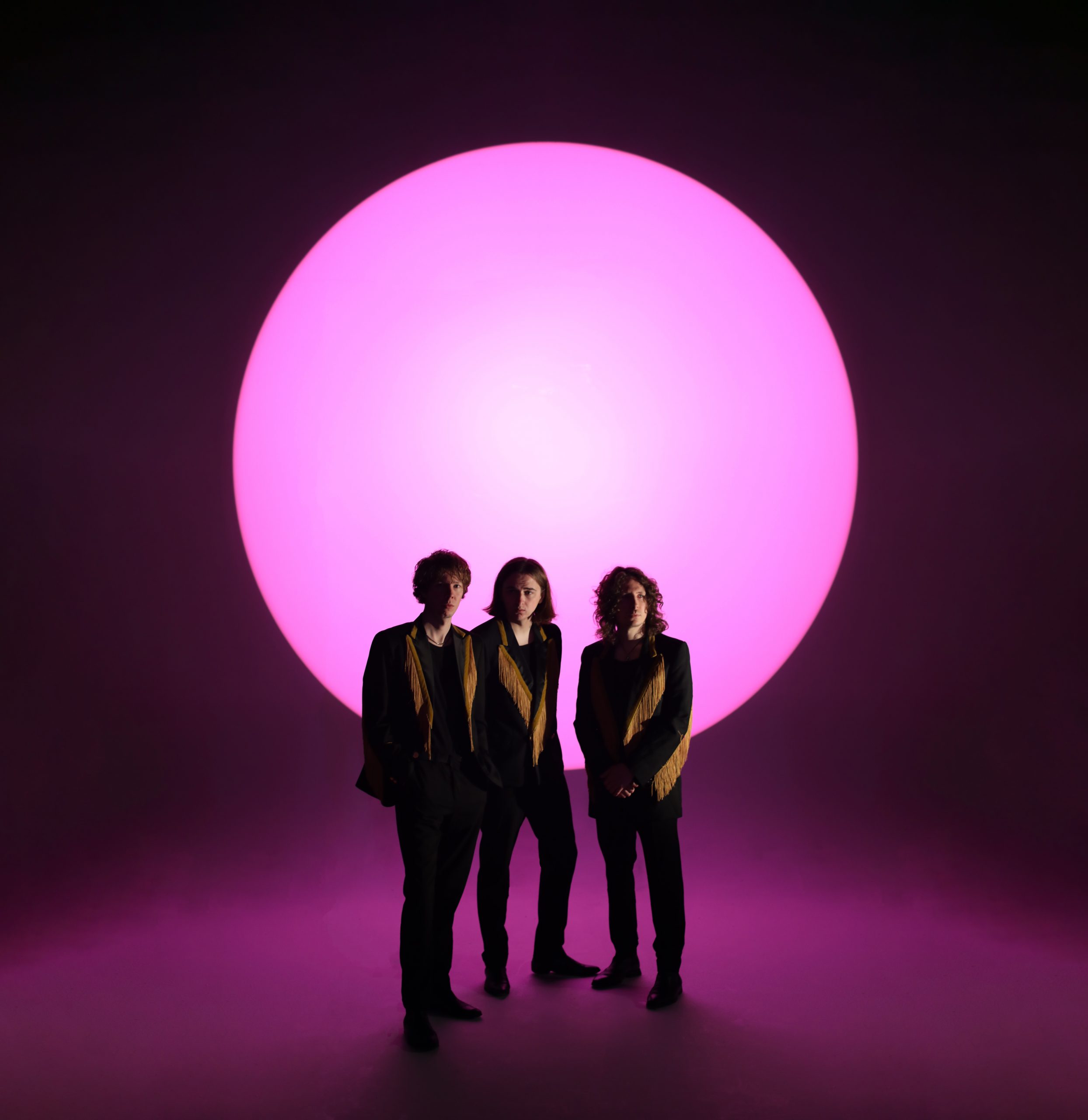 Press photo of The Howlers. Three young man with a giant pink circle behind them.